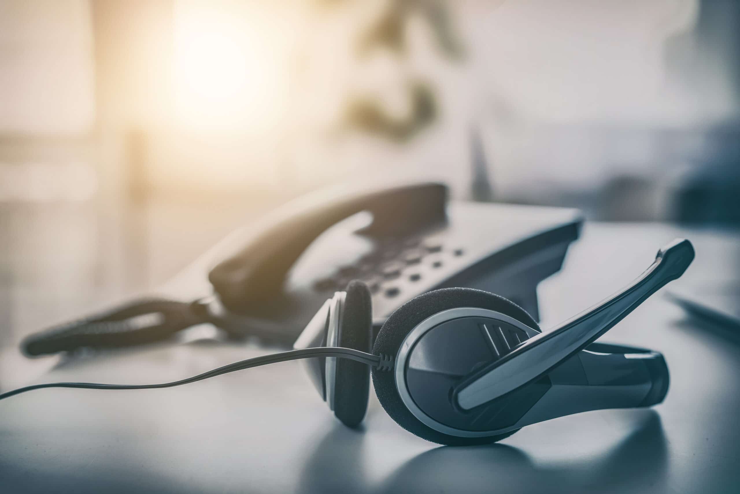 A headset sits next to a telephone in a contact centre