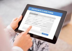 A person holds a tablet displaying an insurance claims form