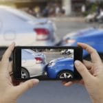 Close up of hands holding a smartphone and taking a photo at the scene of a car accident to submit as first notice of loss for a car insurance claim