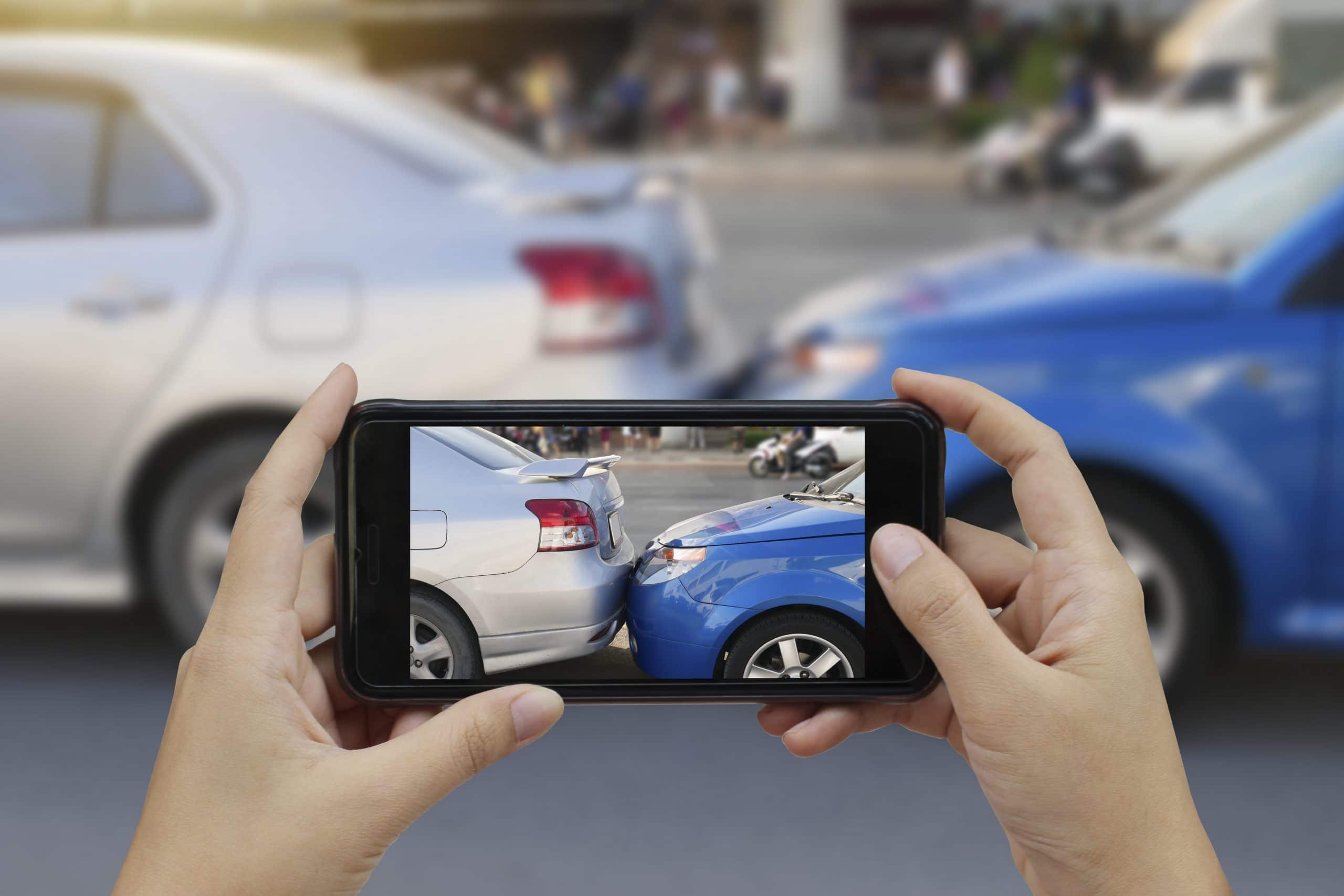 Close up of hands holding a smartphone and taking a photo at the scene of a car accident to submit as first notice of loss for a car insurance claim