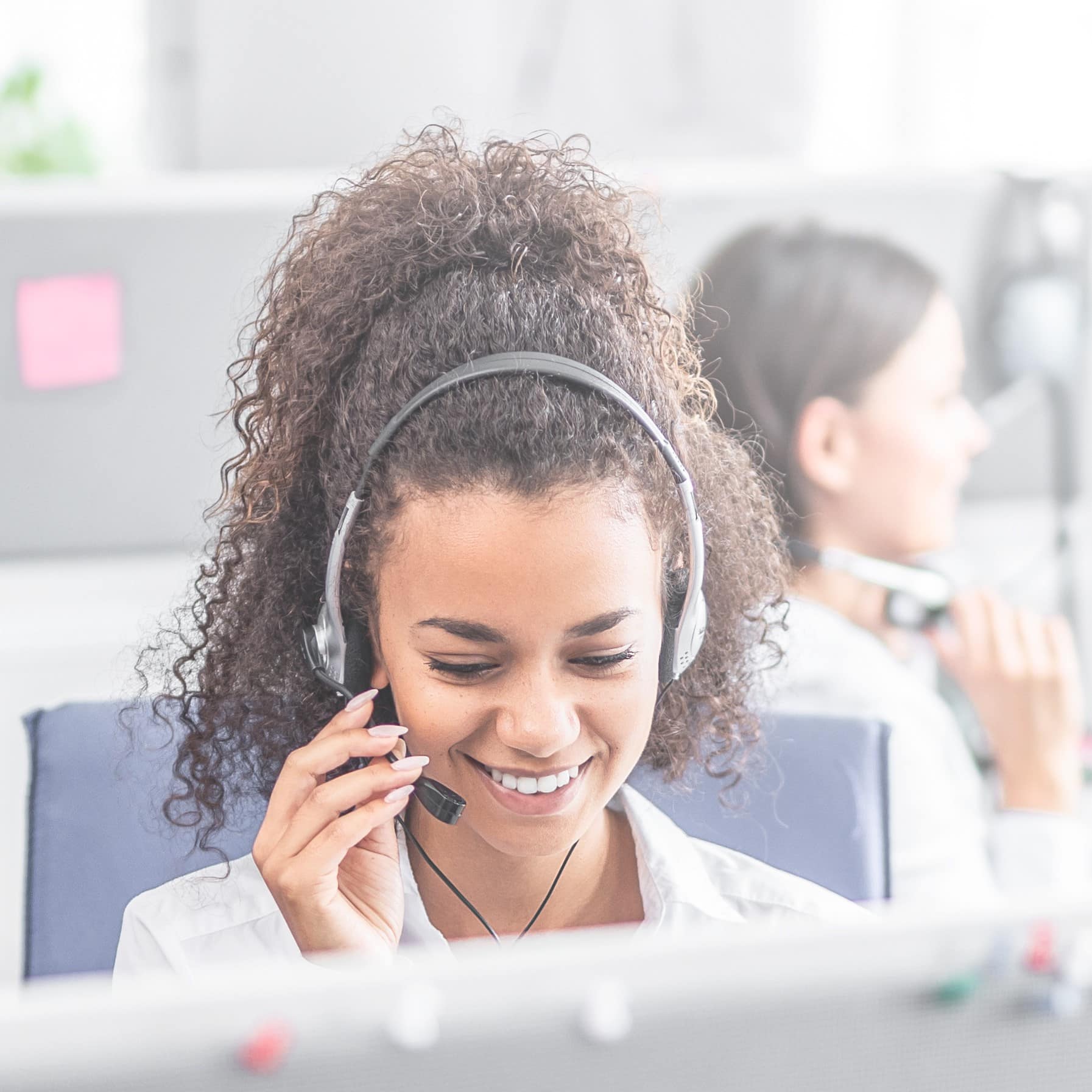 Call center worker accompanied by her team. Smiling customer support operator at work. Young employee working with a headset.