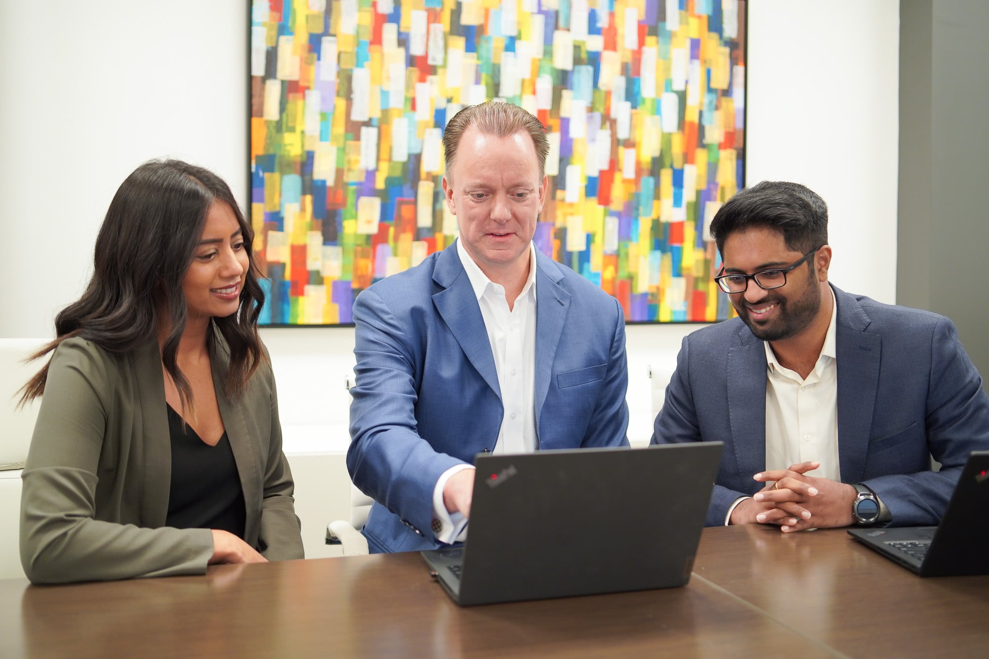 Three team members at a management consulting firm work together on a laptop. Behind them is a colourful abstract painting.