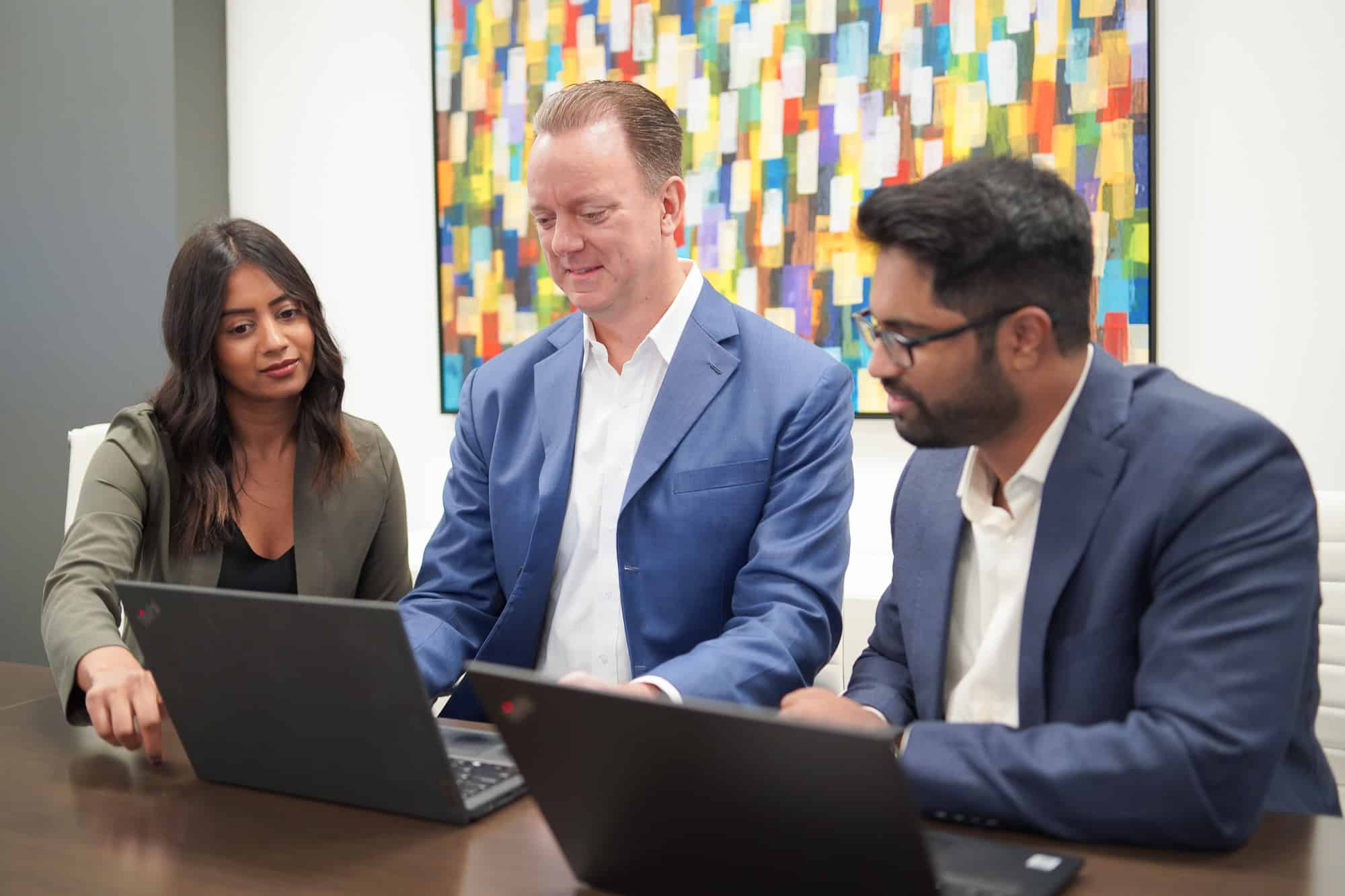 Three coworkers sit at a table with laptops in front of them