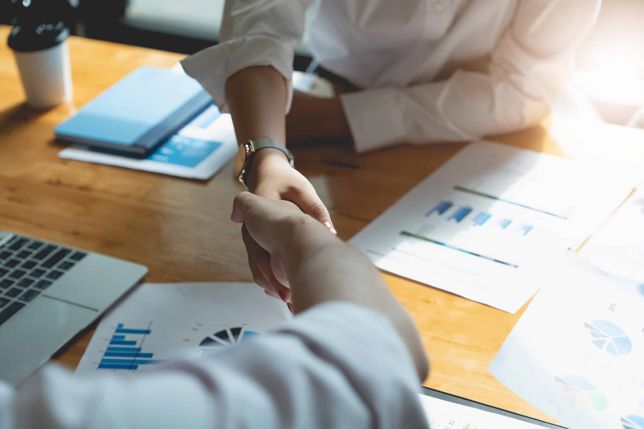 M&A finance synergies - close up of two people shaking hands with revenue information on the table below