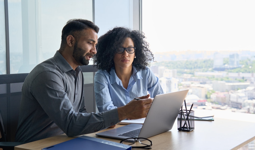 Colleagues talking over a laptop next to a window.