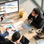Business people at a conference table with paper charts and graphs looking at a gantt chart