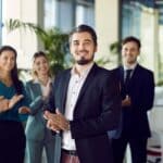A professional portrait of a happy, successful company CEO and business team leader, with a team clapping behind him.