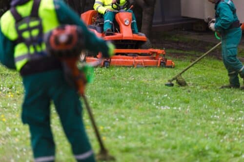 Three landscapers in uniform mowing and cleaning a lawn